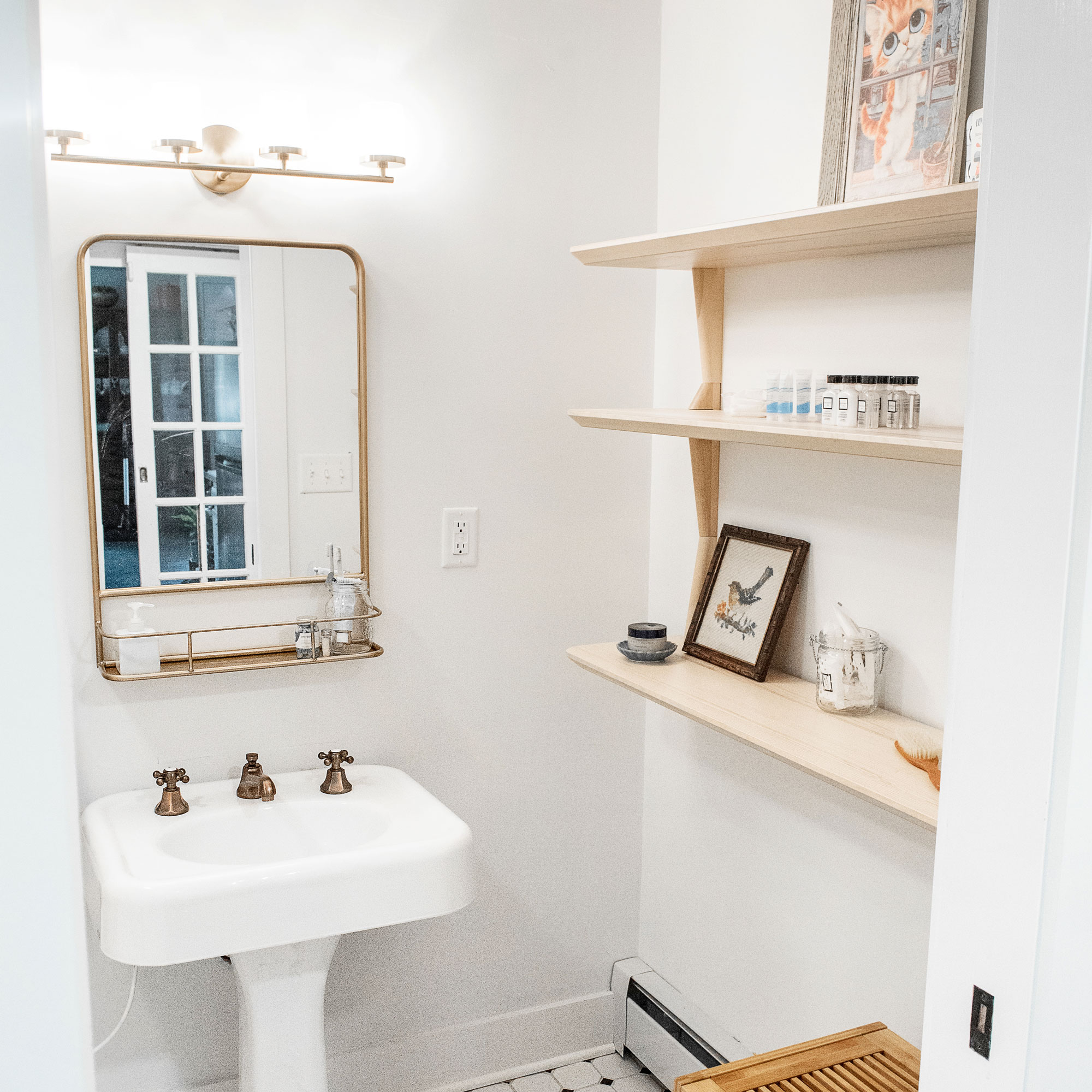 A white bathroom with black and white floor tiles, a pedestal sink with vintage fixtures, and custom shelving.