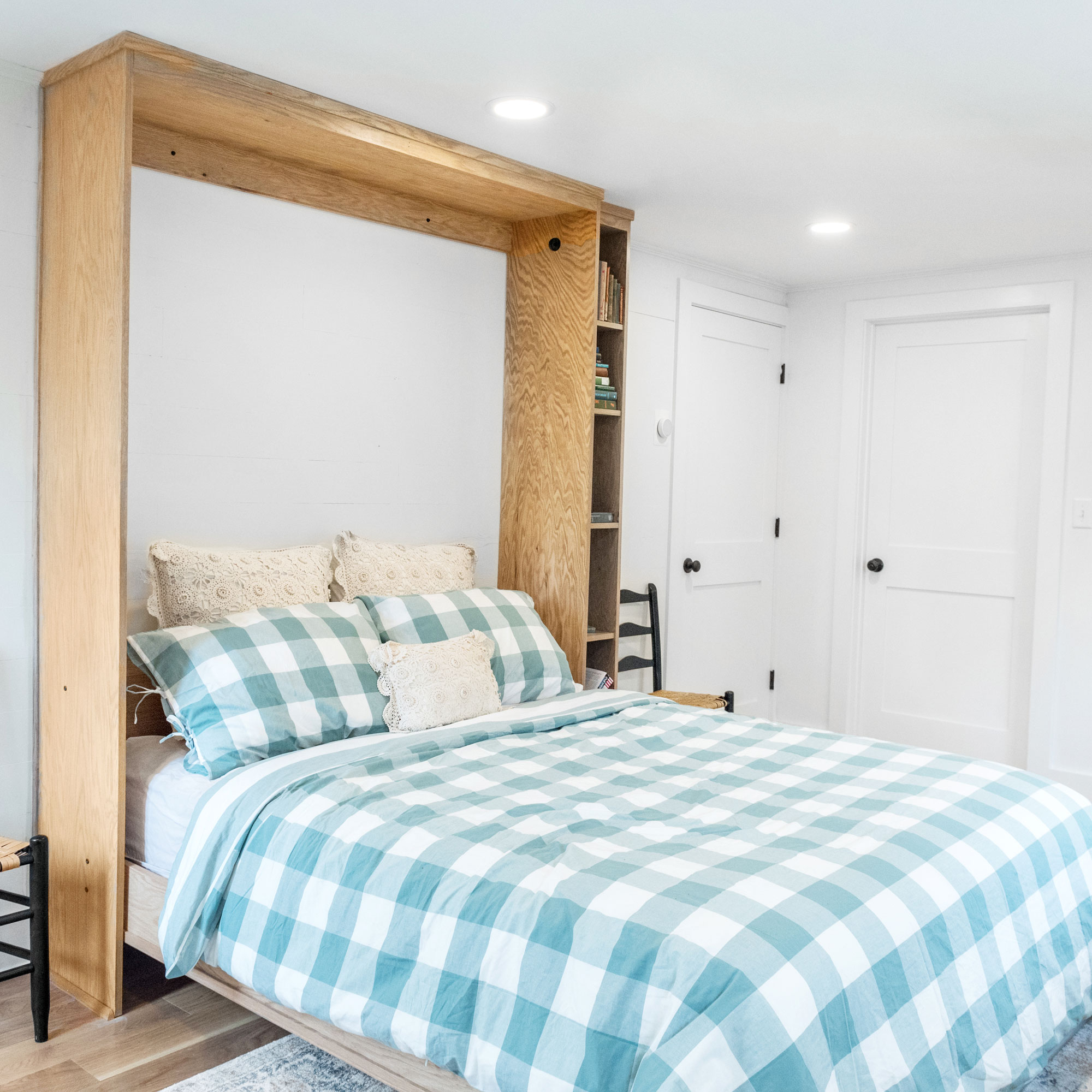 A custom-built Murphy bed with an attached bookcase. The bed is in the down position and covered with a green gingham comforter.